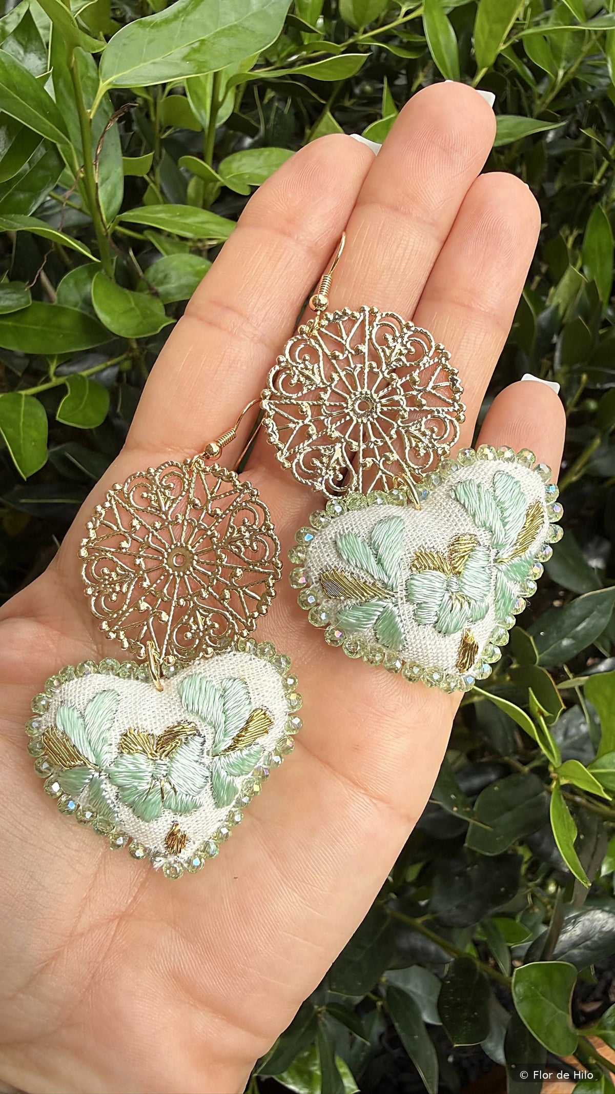 Hand-embroidered heart earrings in mint held in a hand