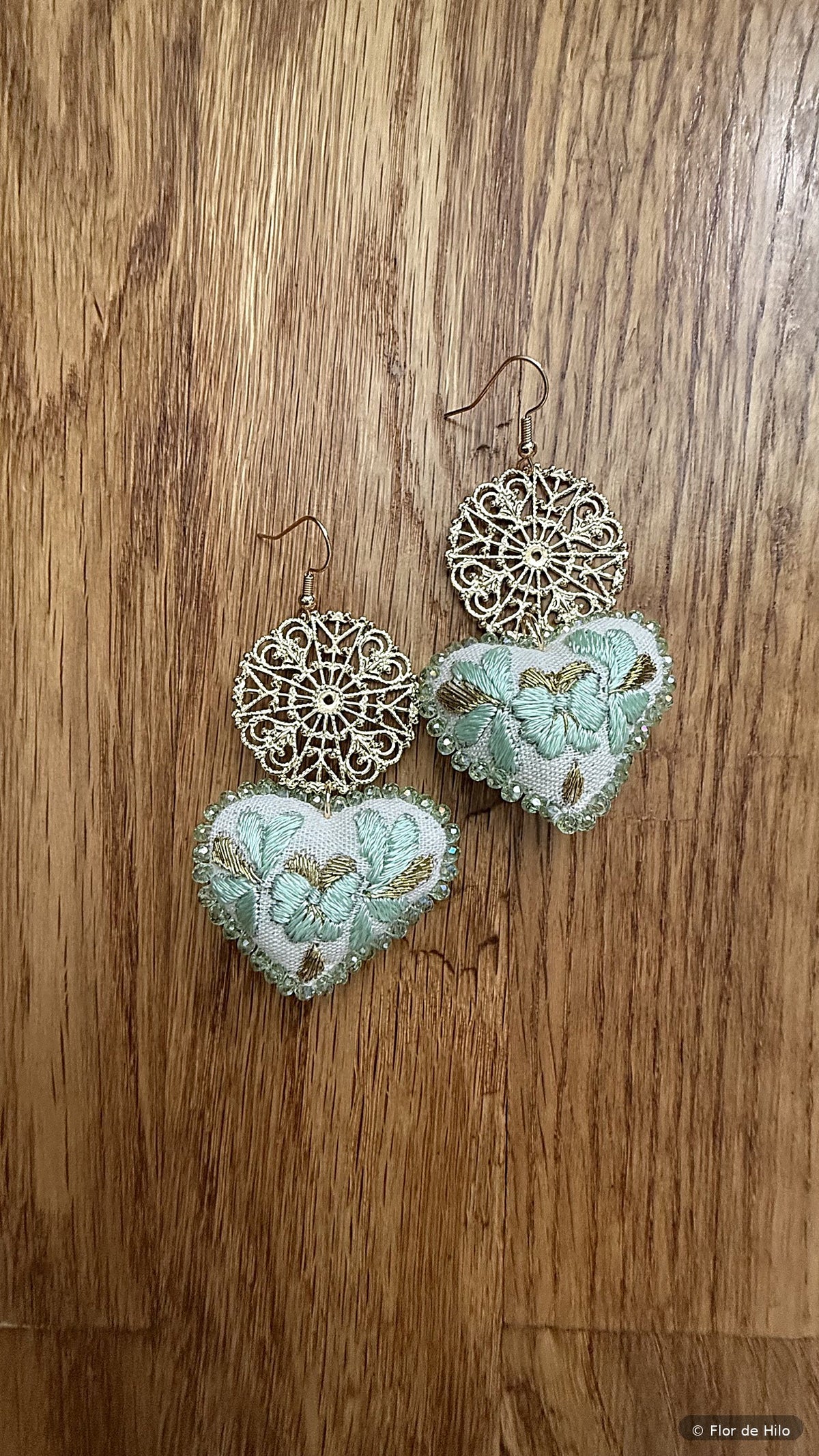 Hand-embroidered heart earrings in mint on a wooden surface