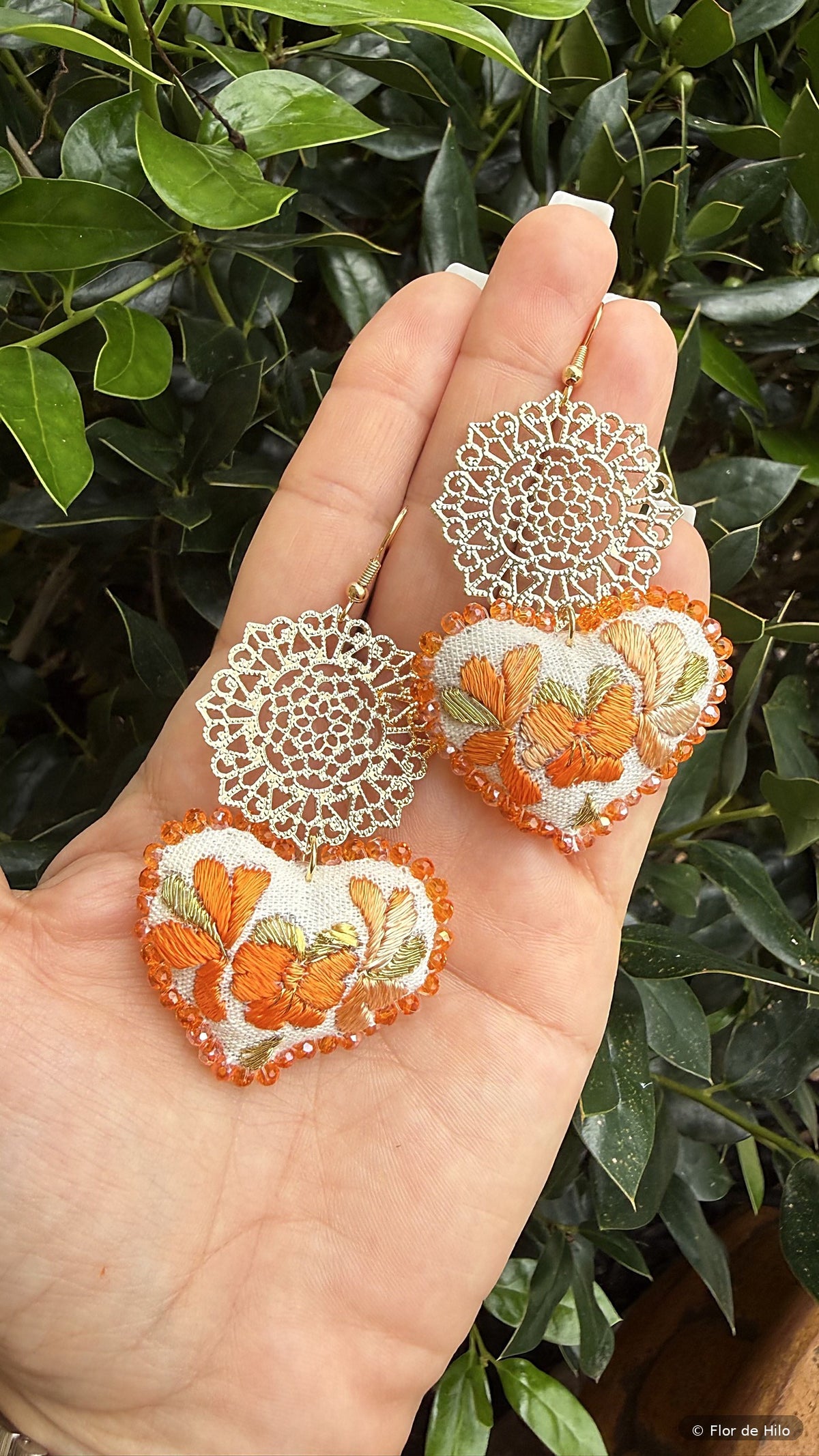 Hand-embroidered heart earrings in orange held in a hand