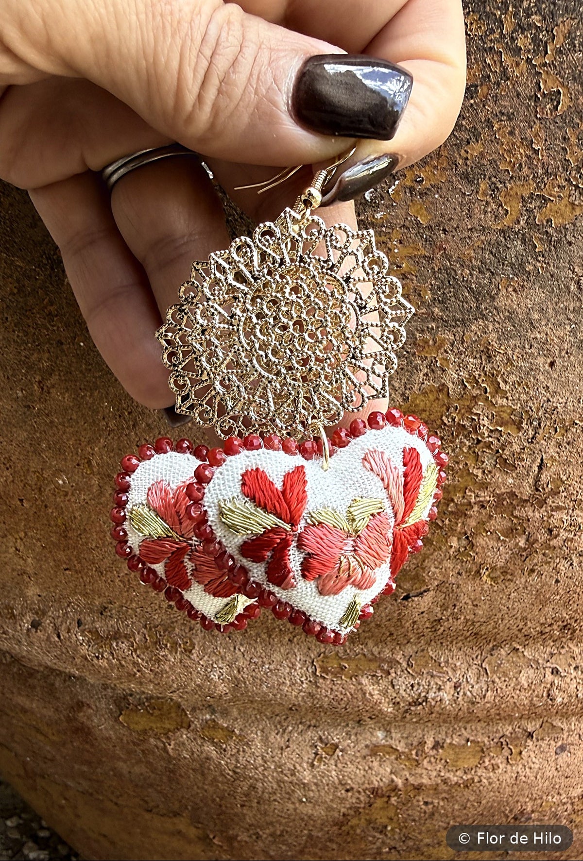 Close-up of red hand-embroidered heart earring with gold-plated filigree detail